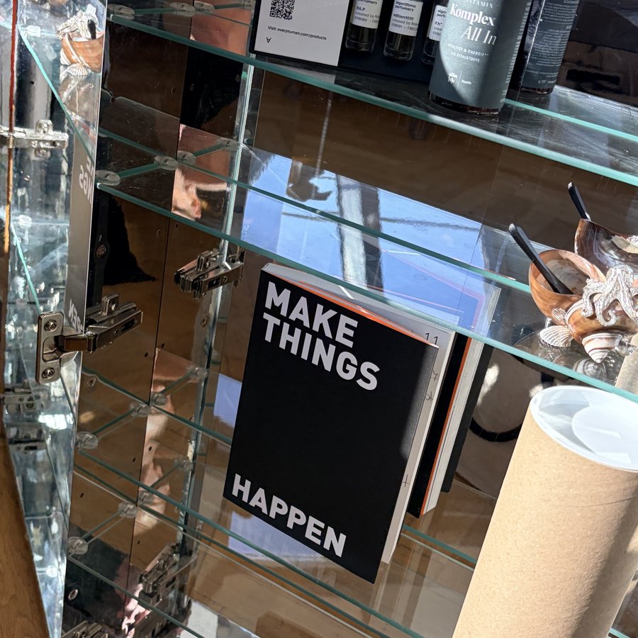 Glasvitrine mit dem Planer Make Things Happen, Papierrollen und Gläsern